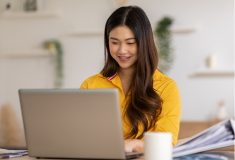 woman wearing yellow blouse, smiling, looking at laptop